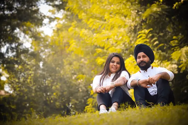 A couple sitting together in a bright field of yellow flowering shrubs, trees behind them.